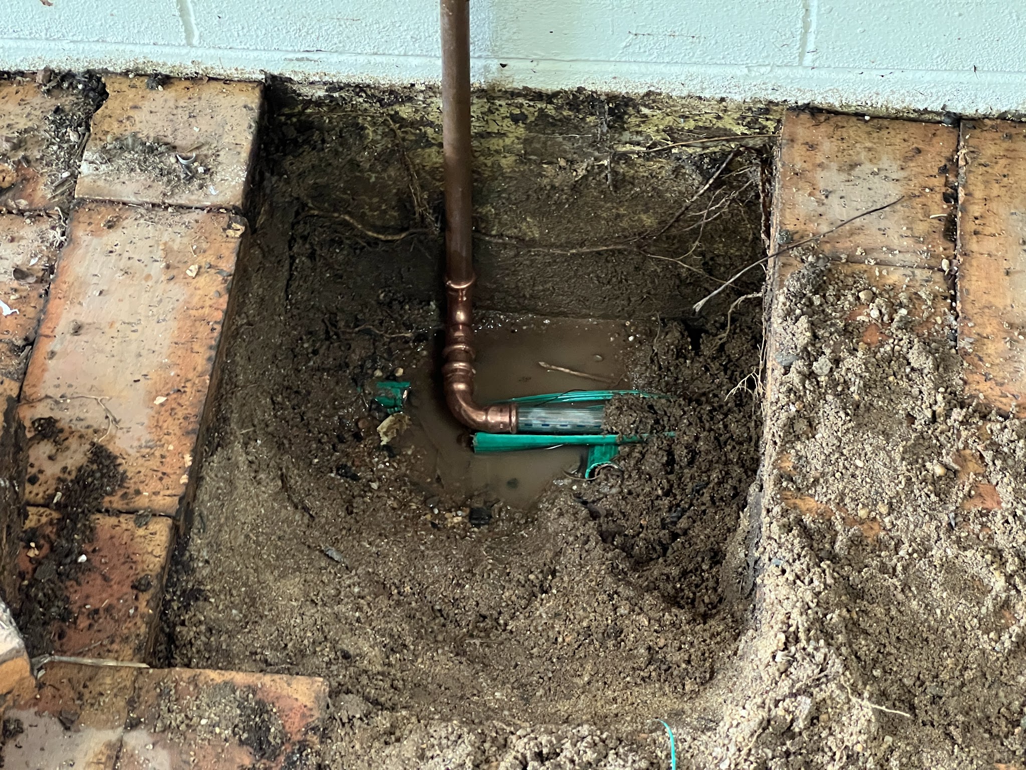 An excavated trench under lifted pavers showing a repaired underground copper water service