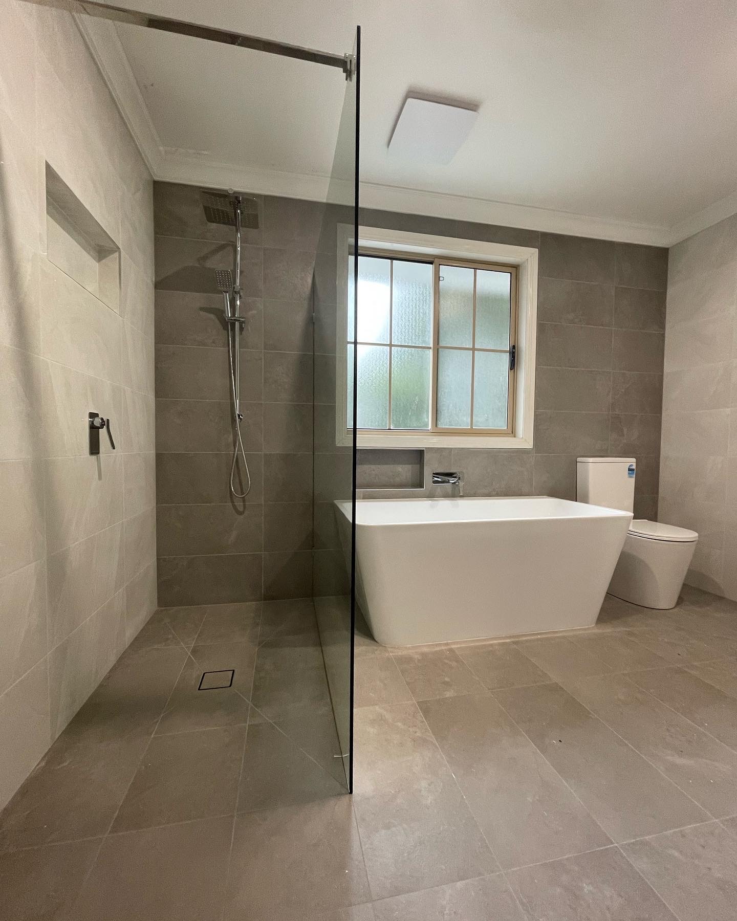 A finished bathroom renovation with a frameless walk-in shower, linear floor drain, freestanding bath and large format tiles