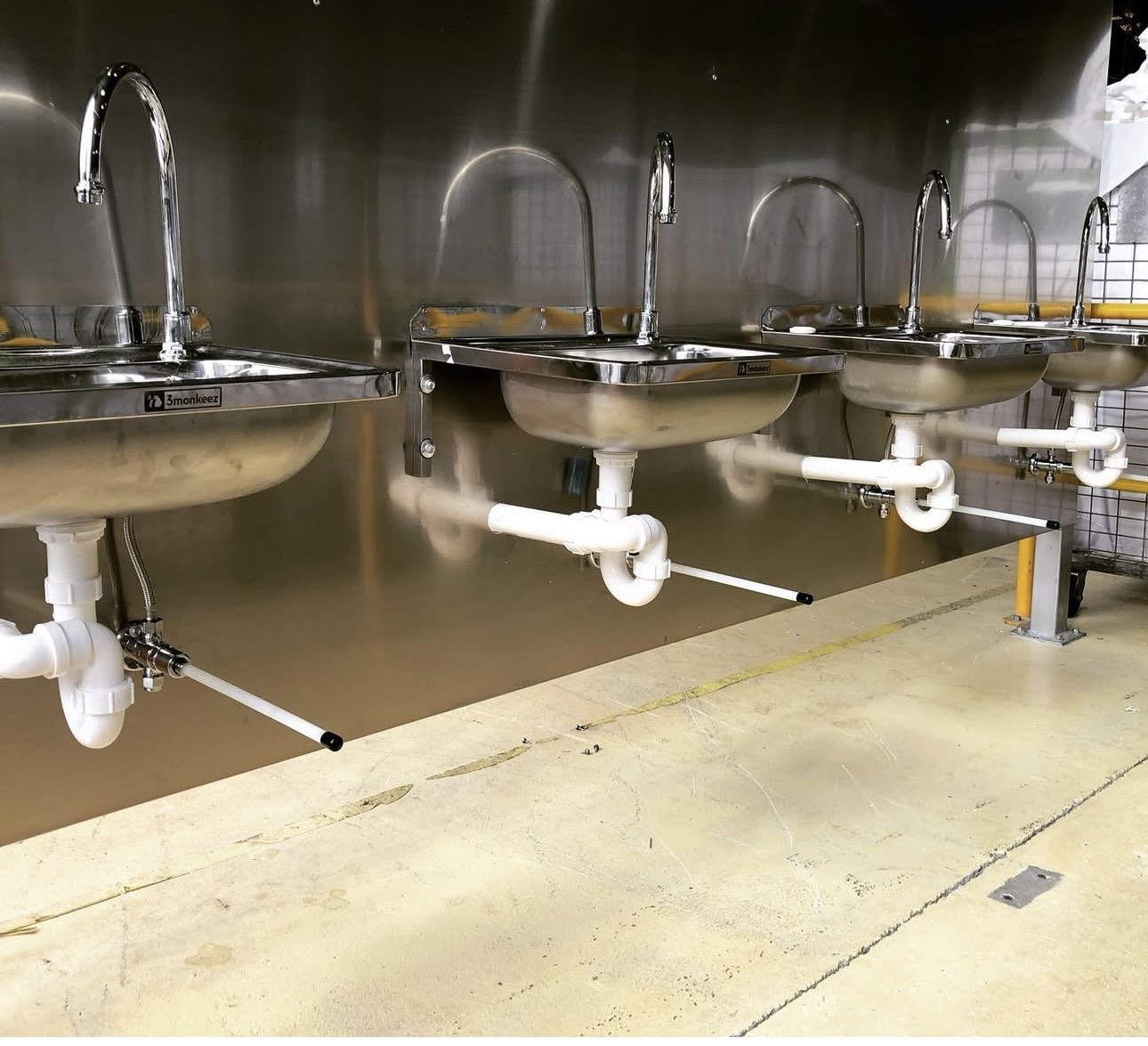A bank of four stainless steel wall hung hand basins with gooseneck tapware in a commercial fit out