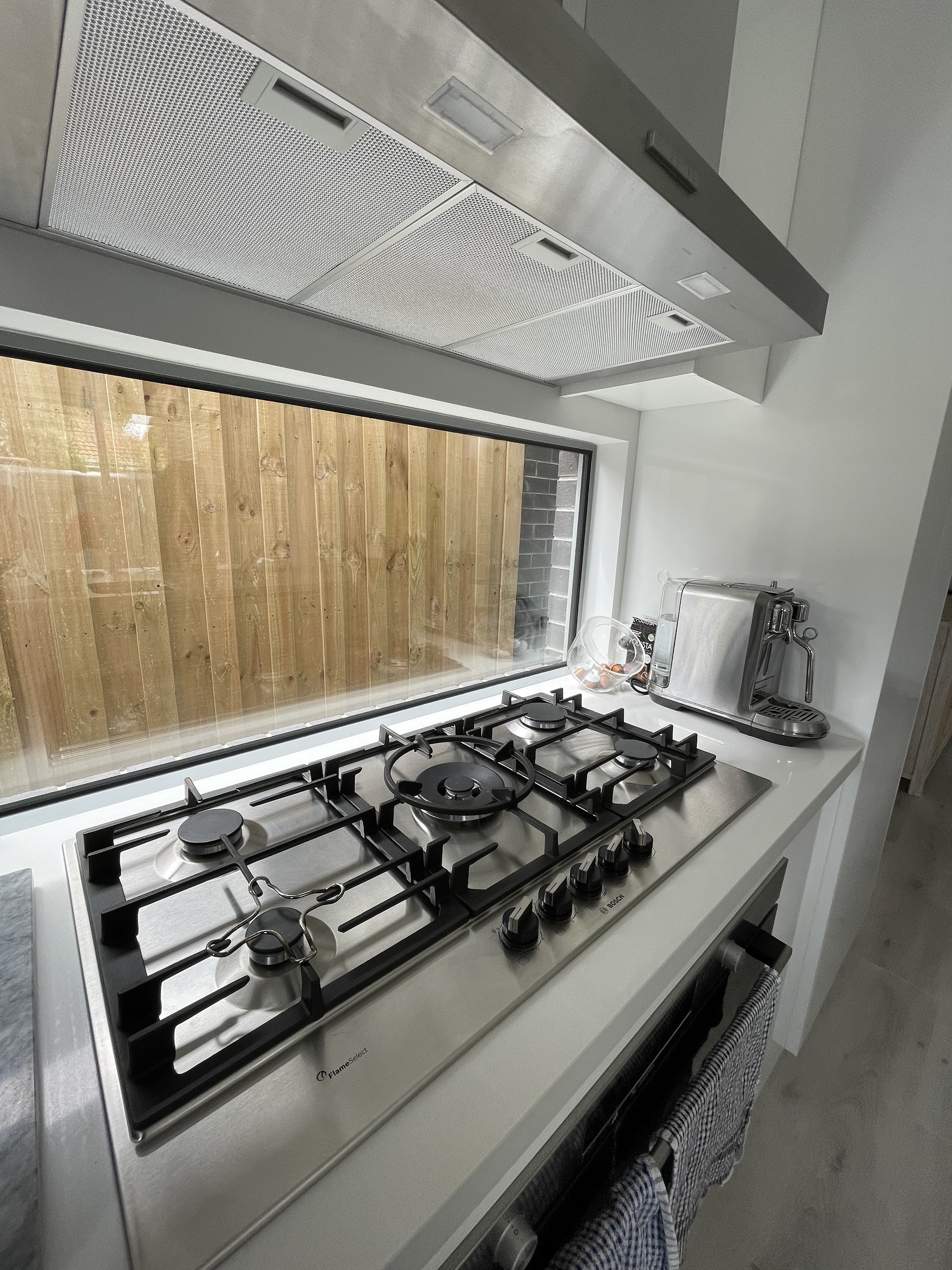 An installed Bosch five burner gas cooktop with a stainless steel canopy rangehood above it